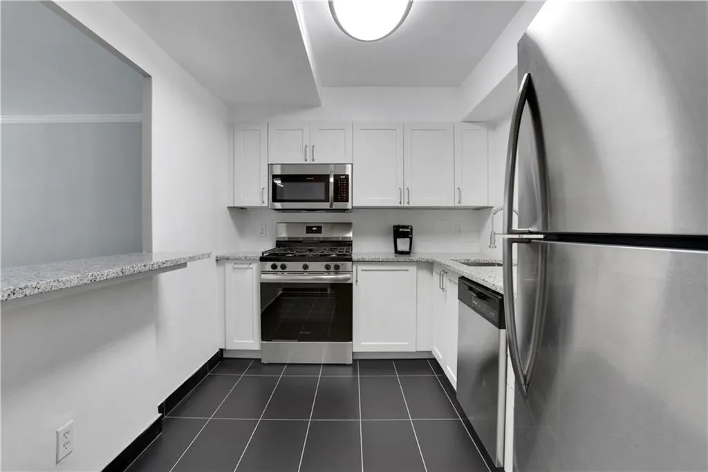Kitchen featuring stainless steel appliances, white cabinets, dark tile patterned floors, light stone countertops, and tasteful backsplash