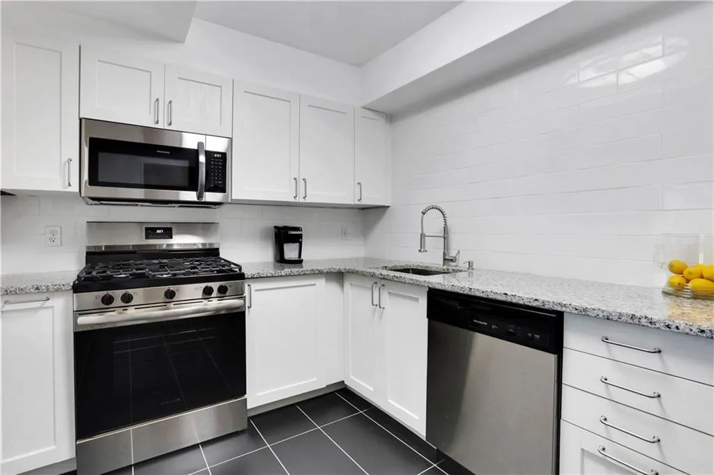 Kitchen featuring stainless steel appliances, tasteful backsplash, white cabinetry, light stone counters, and dark tile patterned floors