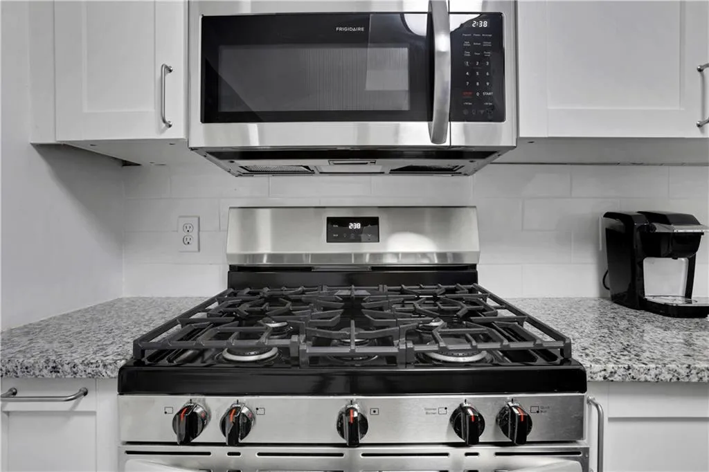 Kitchen view of stainless steel appliances, light stone countertops, backsplash, and white cabinets