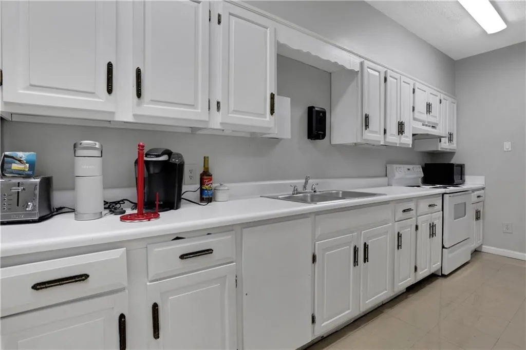 Kitchen with electric stove, light countertops, white cabinetry, and black microwave