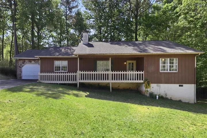 Single-story residence featuring a covered front porch with white railings, a stone-clad garage with a white door, and a prominent chimney