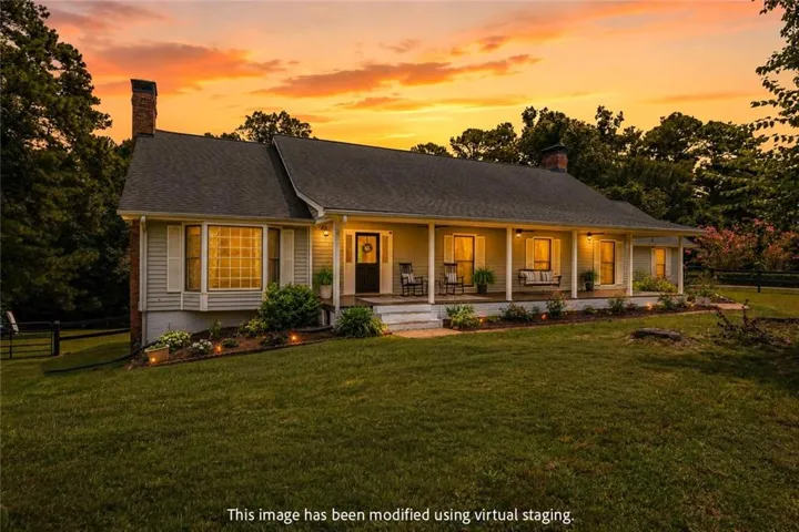 Classic ranch-style residence featuring a covered front porch, bay window with shutters, brick chimney, and landscape lighting