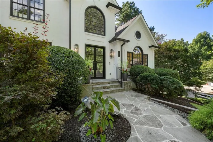 White exterior with black-framed windows, stone walkway, stone steps, and integrated wall sconces