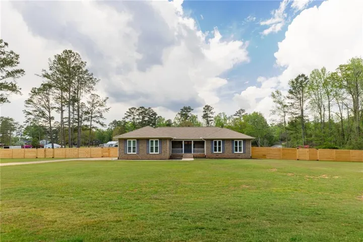 Brick exterior residence featuring a covered front porch, a wood privacy fence, and a spacious front lawn