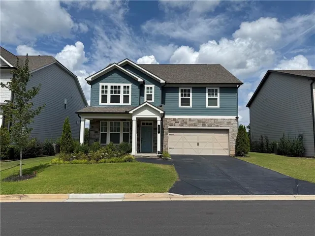 Two-story residence featuring a stone and siding exterior, an attached two-car garage, covered entry with columns, and a landscaped front yard