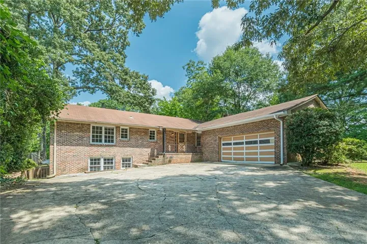 Brick exterior with a two-car garage, mature trees, and a spacious concrete driveway
