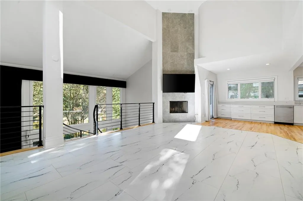 Unfurnished living room with a fireplace, plenty of natural light, high vaulted ceiling, and light marble finish flooring Unfurnished living room with a fireplace, plenty of natural light, high vaulted ceiling, and light marble finish flooring