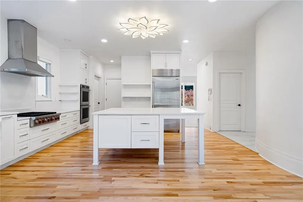 Kitchen featuring island range hood, white cabinets, a kitchen bar, light wood-type flooring, and recessed lighting Kitchen featuring island range hood, white cabinets, a kitchen bar, light wood-type flooring, and recessed lighting