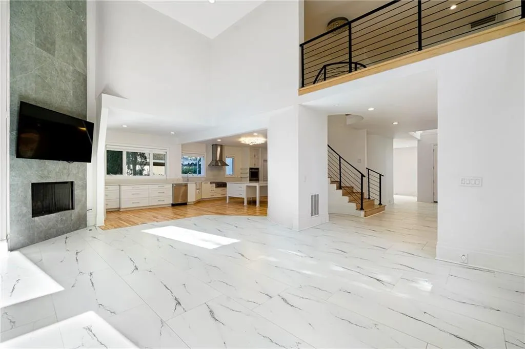 Unfurnished living room with a high ceiling, recessed lighting, light marble finish floors, a fireplace, and stairs Unfurnished living room with a high ceiling, recessed lighting, light marble finish floors, a fireplace, and stairs