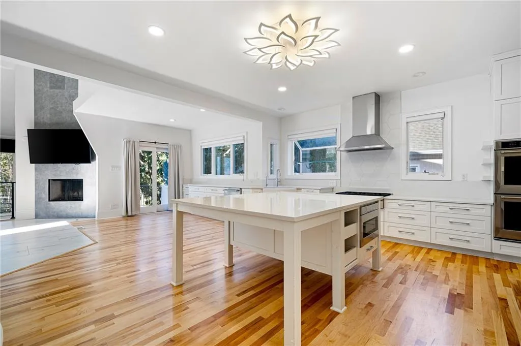 Kitchen featuring healthy amount of natural light, light wood-style floors, white cabinets, wall chimney range hood, and recessed lighting Kitchen featuring healthy amount of natural light, light wood-style floors, white cabinets, wall chimney range hood, and recessed lighting