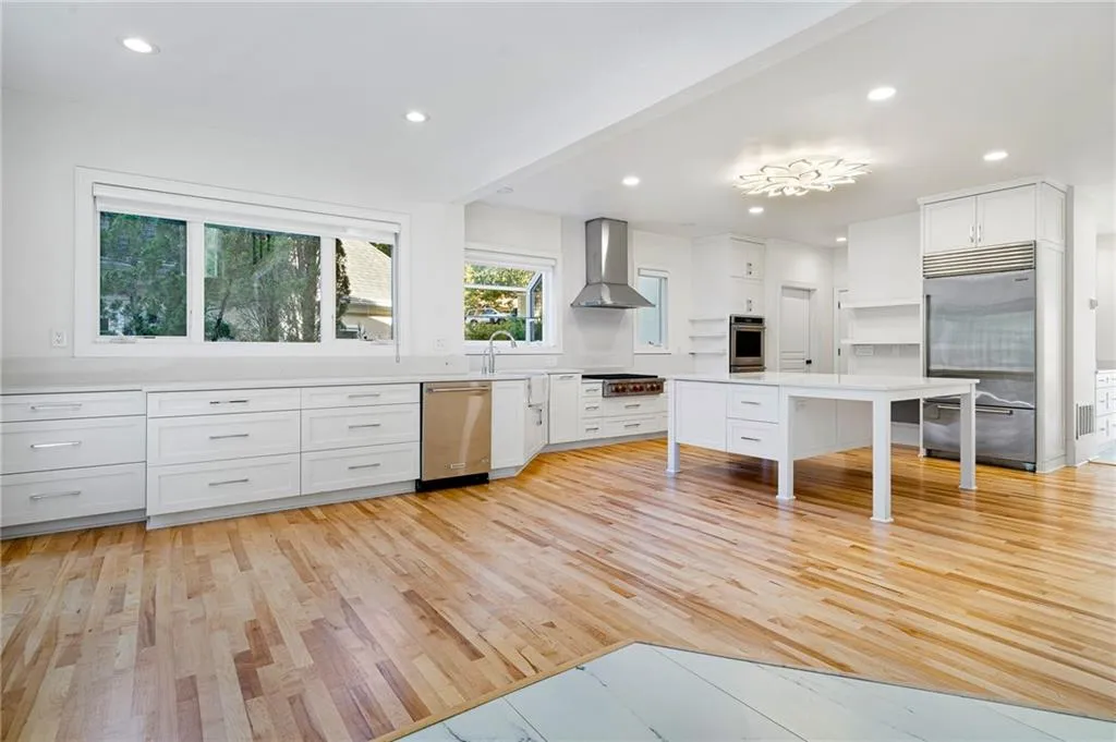 Kitchen with recessed lighting, light wood finished floors, white cabinets, stainless steel appliances, and wall chimney exhaust hood Kitchen with recessed lighting, light wood finished floors, white cabinets, stainless steel appliances, and wall chimney exhaust hood