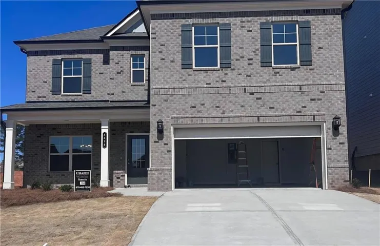 Two-story brick exterior with dark shutters, covered front porch with white columns, attached two-car garage, and concrete driveway
