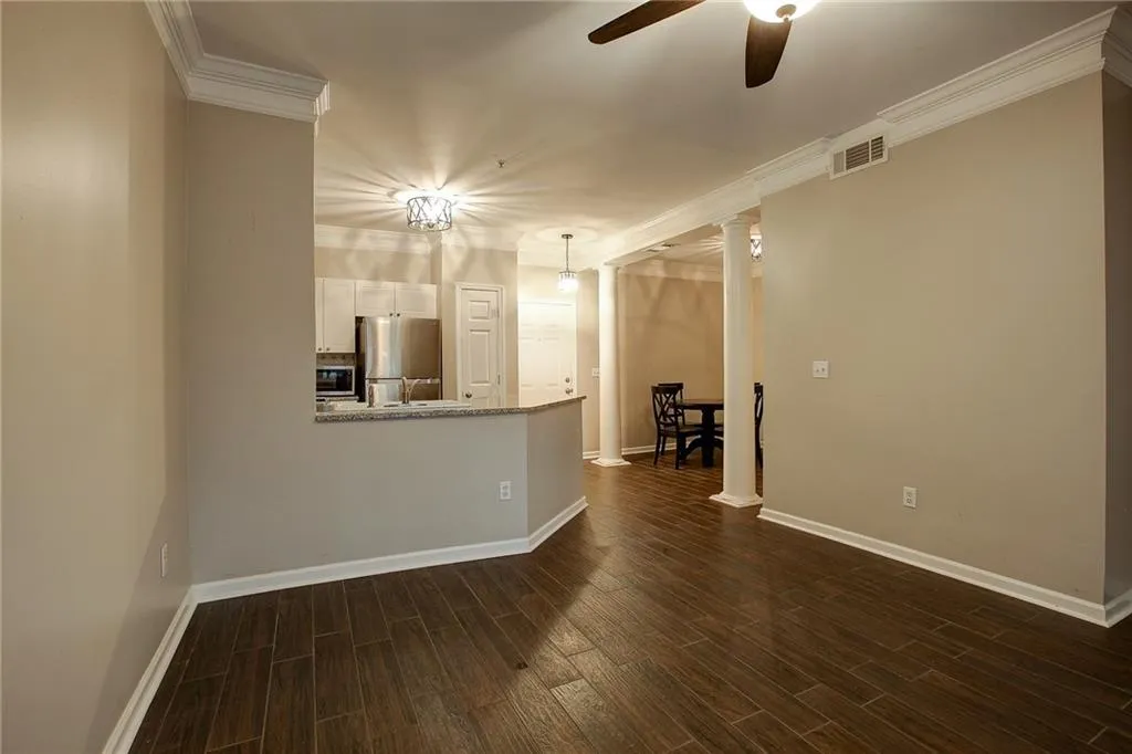 Unfurnished living room featuring a ceiling fan, wood tiled floors, crown molding, and ornate columns