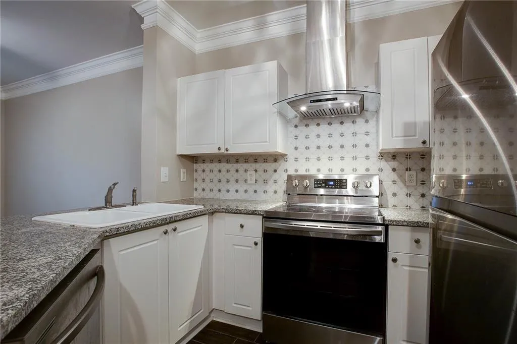 Kitchen featuring white cabinets, stainless steel appliances, exhaust hood, ornamental molding, and backsplash