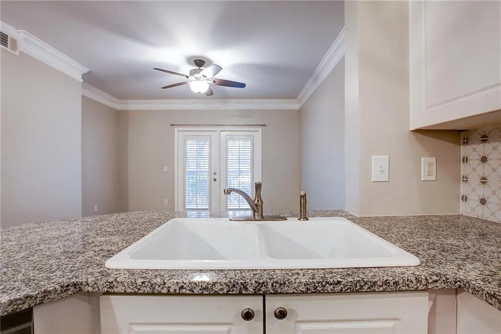 Kitchen view of crown molding, white cabinetry, decorative backsplash, a ceiling fan, and light stone counters