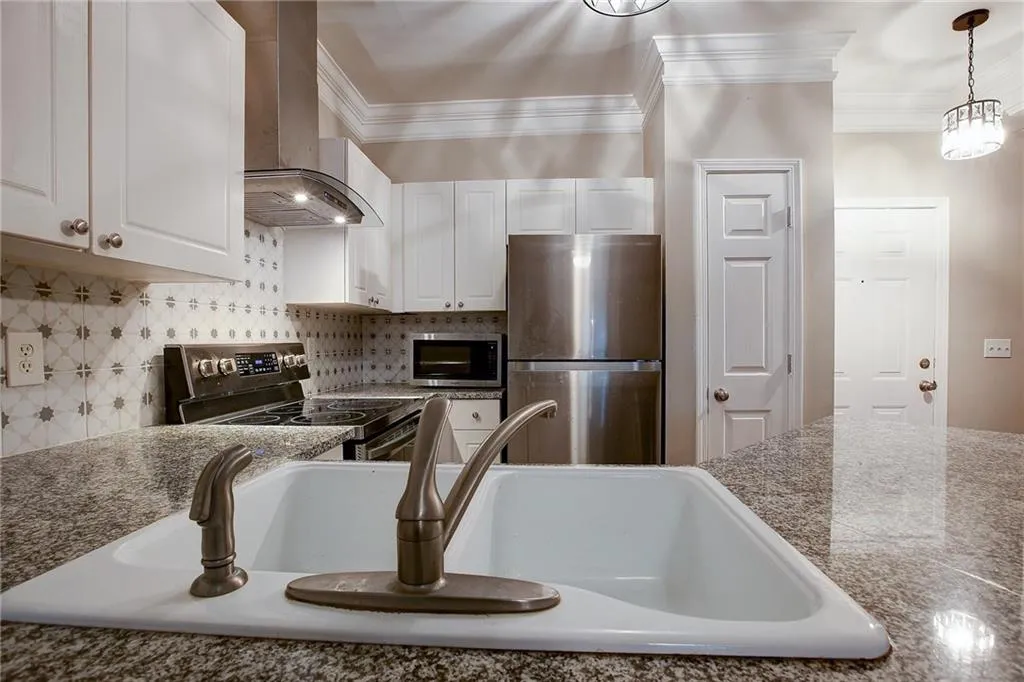 Kitchen featuring stainless steel appliances, exhaust hood, white cabinets, crown molding, and hanging light fixtures