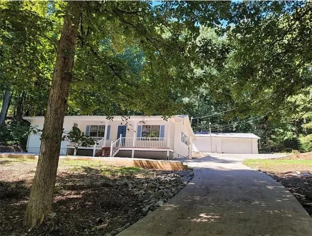 White exterior with light blue shutters, front porch with white railing, and a paved driveway