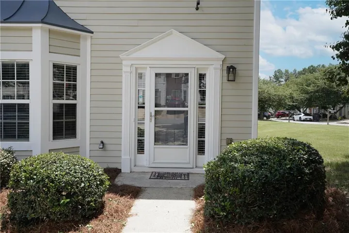 Exterior entrance featuring a decorative pediment over the front door, a black wall sconce, and a bay window with a dark metal roof accent