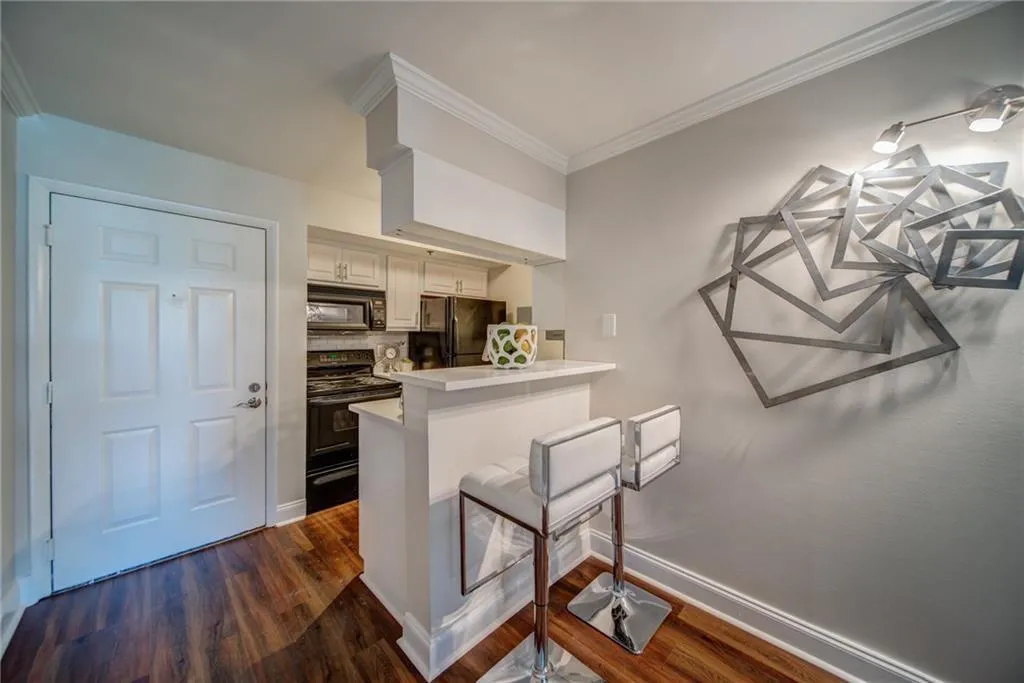 Kitchen with black appliances, a breakfast bar area, a peninsula, dark wood-style flooring, and light countertops