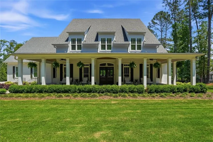 Expansive front lawn with layered landscaping, full-width covered porch, multiple dormer windows, and a double-door entryway
