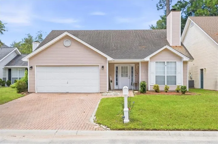 Front exterior with light-colored siding, an attached garage, a brick paver driveway, and a covered entry