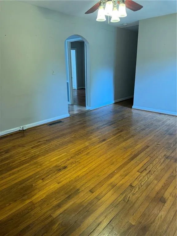 Empty room featuring arched walkways, dark wood finished floors, and ceiling fan