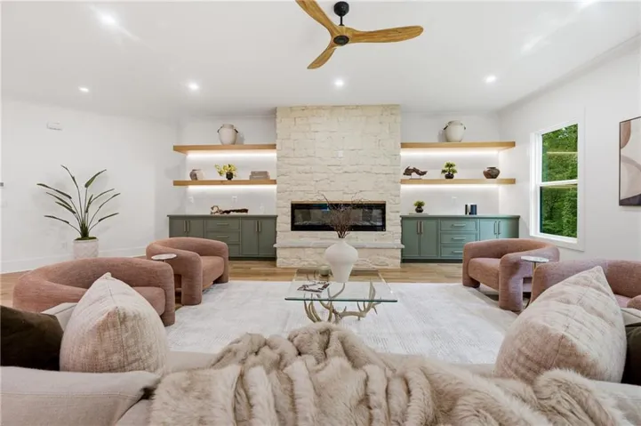 Stone-clad fireplace with an integrated electric insert, wood-finish flooring, recessed lighting, and a ceiling fan