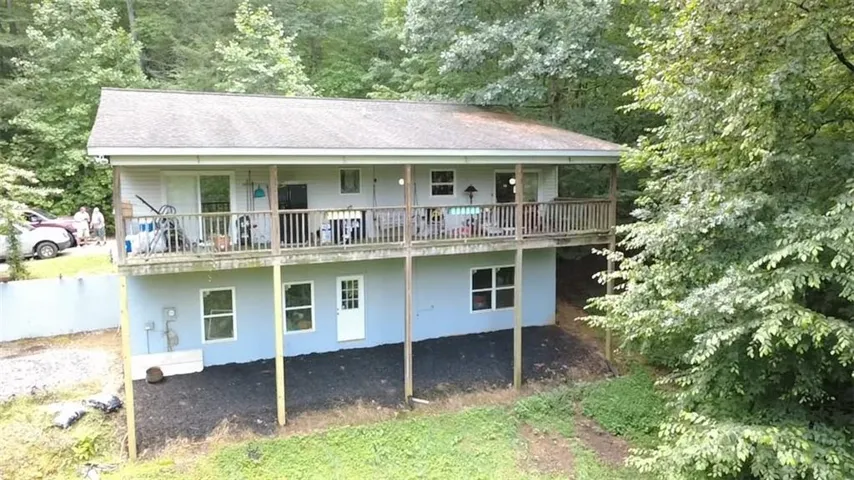 Two-story residence featuring a full-width upper deck with wood railing, lower-level walkout access, and a surrounding wooded landscape