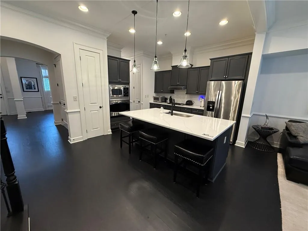 Kitchen with dark cabinetry, arched walkways, decorative light fixtures, a kitchen breakfast bar, and recessed lighting