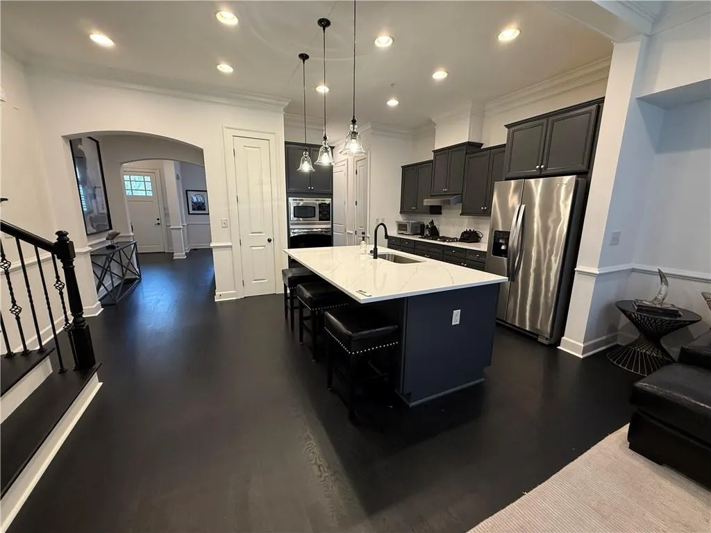 Kitchen with dark cabinets, arched walkways, a kitchen island with sink, pendant lighting, and recessed lighting