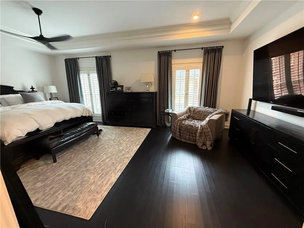 Bedroom with a raised ceiling, dark wood-style flooring, and ceiling fan