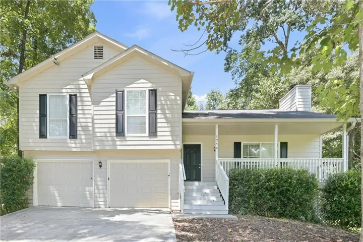 Split-level residence featuring light-colored siding, a covered front porch with white railings, a dark entry door, and a two-car garage