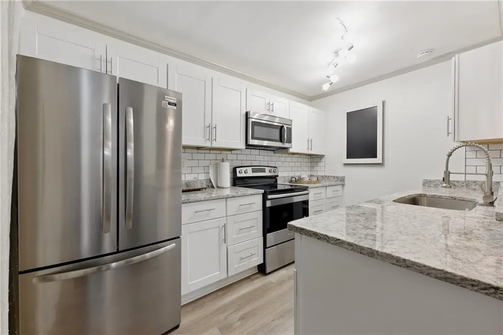 Kitchen featuring stainless steel appliances, tasteful backsplash, white cabinets, light stone countertops, and ornamental molding