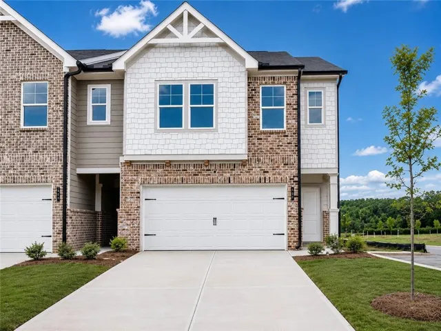Modern townhome exterior featuring a two-car garage with decorative hardware, brick and horizontal siding accents, shake siding on the gables, and a concrete driveway