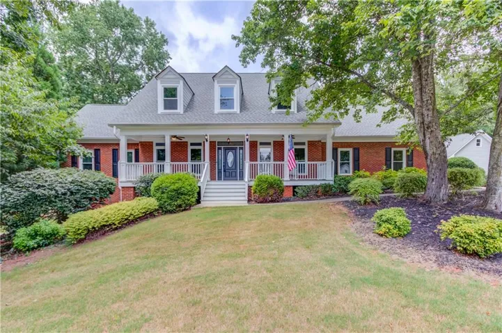Brick exterior with dormer windows and a covered front porch featuring white columns and railings