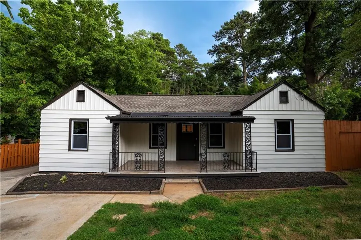 Charming single-story residence featuring white horizontal siding, a covered front porch with wrought iron railing, dark-trimmed windows, a shingle roof, and a fenced side yard