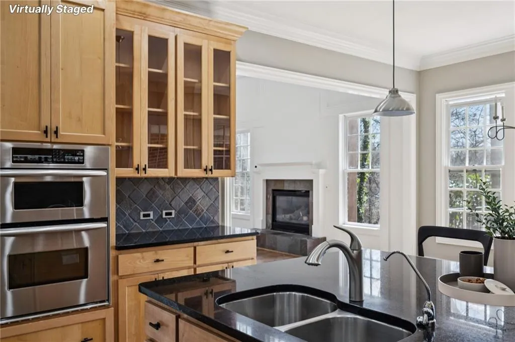 Kitchen featuring stainless steel double oven, light wood finish cabinetry, dark stone counters, ornamental molding, and backsplash