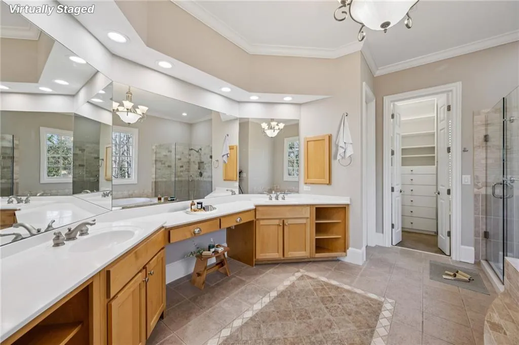 Bathroom featuring hanging lights, a shower stall, crown molding, two vanities, and a spacious closet