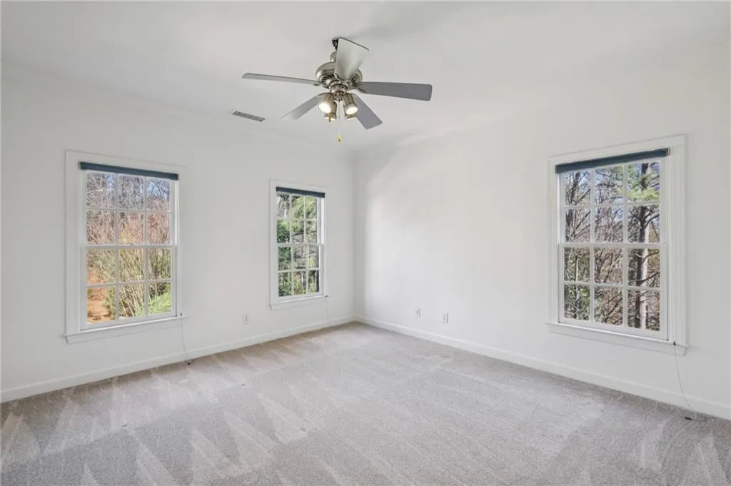 Empty room featuring ornamental molding, plenty of natural light, light carpet, and ceiling fan