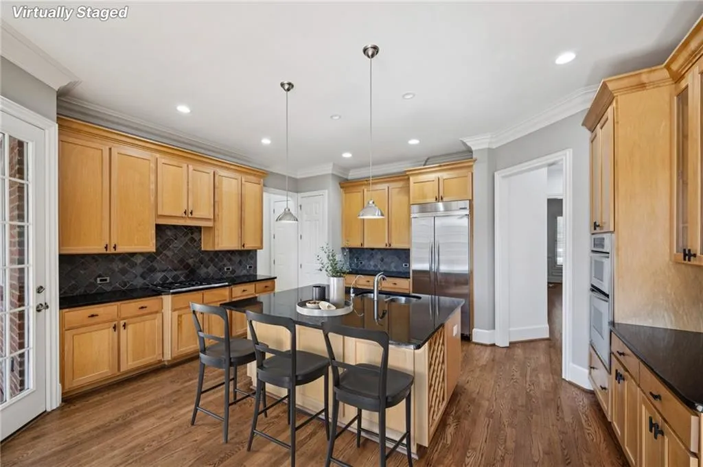 Kitchen with a kitchen island with sink, ornamental molding, decorative light fixtures, dark wood-type flooring, and a breakfast bar