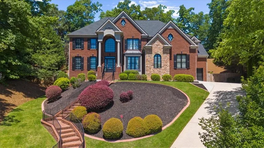 Two-story brick facade featuring stone accents, a prominent arched window, and a multi-tiered front walkway with wrought iron railings