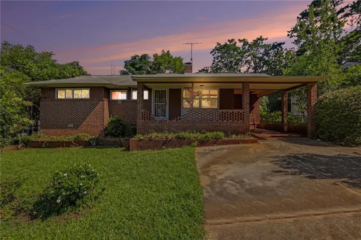 Brick ranch home with covered front porch, expansive lawn, and mature landscaping