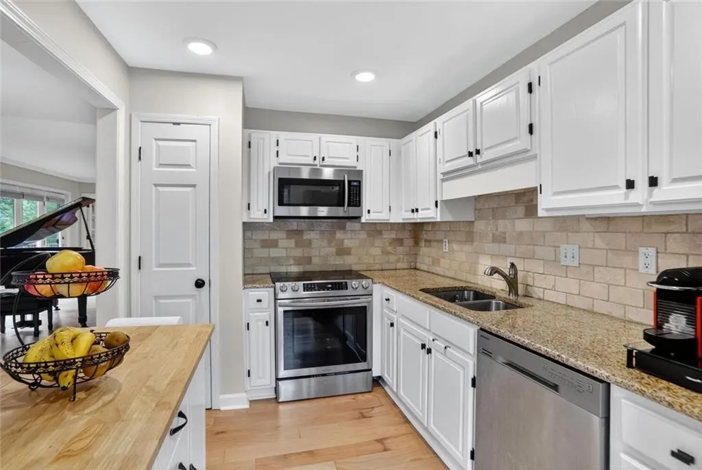 Kitchen with appliances with stainless steel finishes, white cabinets, tasteful backsplash, light wood-style floors, and light stone counters