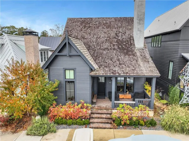 Gabled roofline with wood shake shingles, dark-toned siding, covered front porch, brick entry stairs, and established landscaping