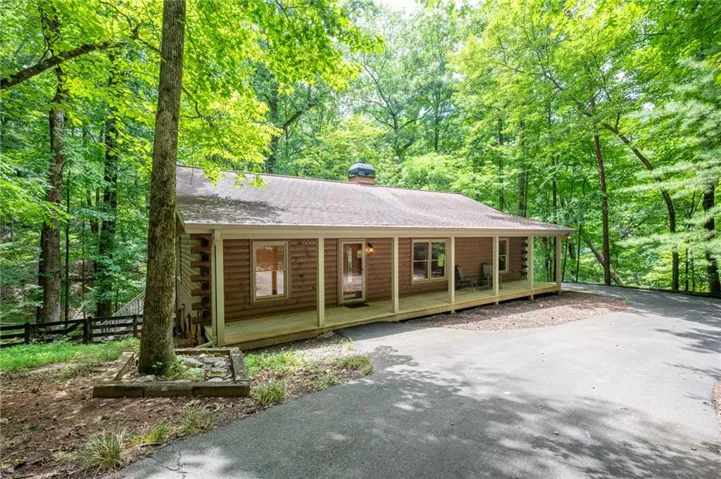 Log cabin exterior featuring a covered porch spanning the facade, a shingle roof, and a paved driveway