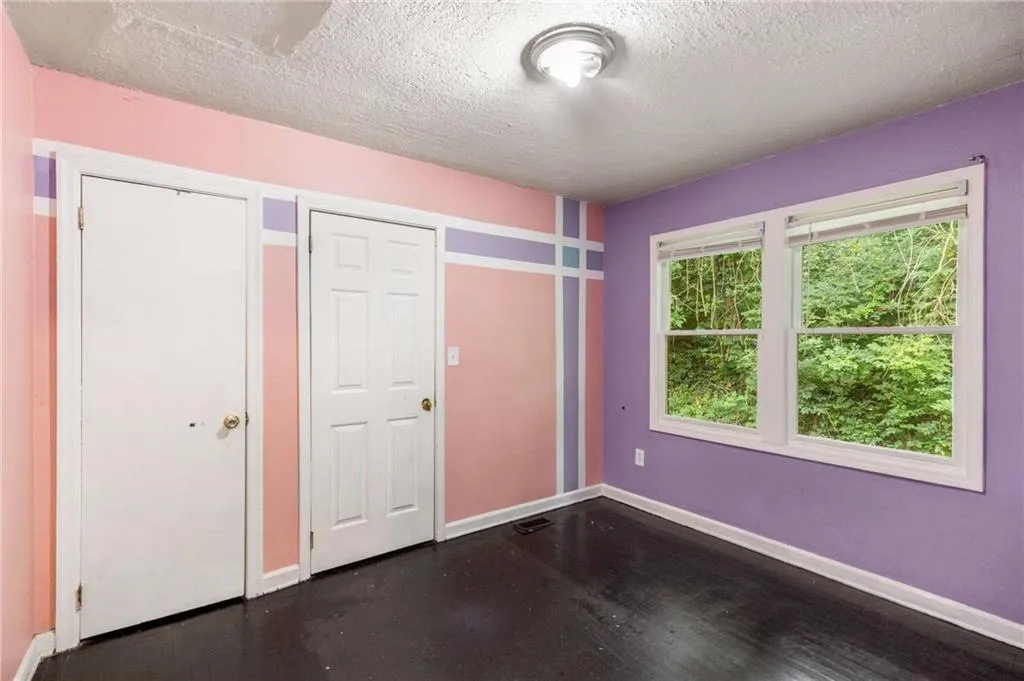 Unfurnished bedroom featuring a textured ceiling, dark wood-style floors, and two closets