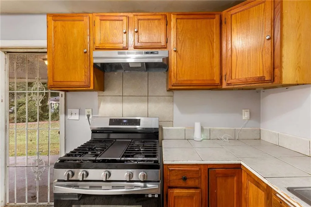 Kitchen with gas range, brown cabinetry, under cabinet range hood, and tile countertops