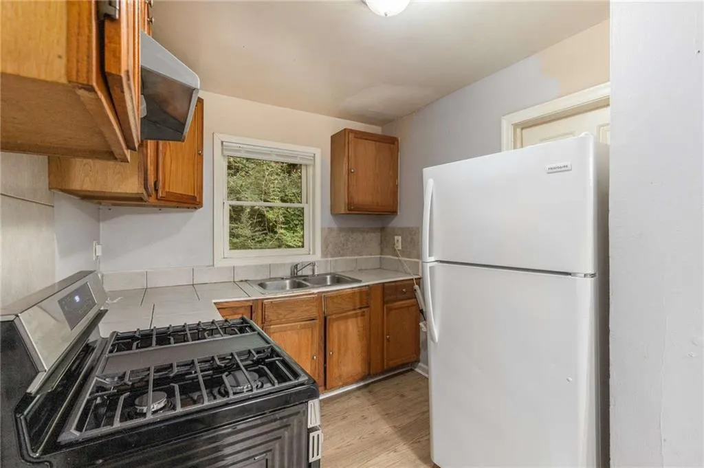 Kitchen with freestanding refrigerator, stainless steel gas range oven, brown cabinets, and light countertops
