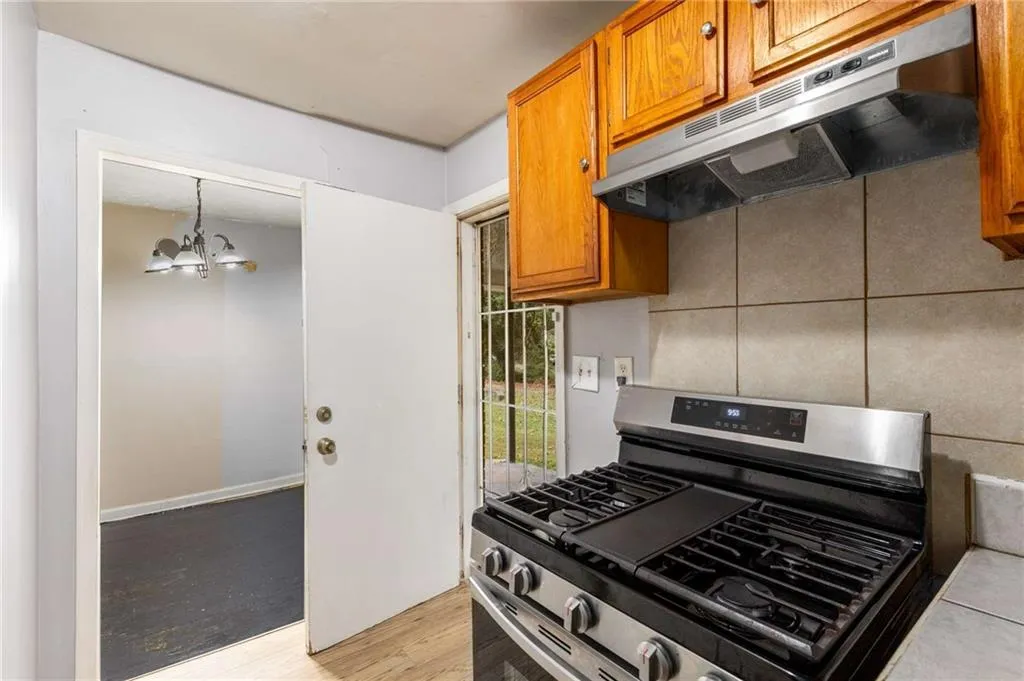Kitchen featuring stainless steel range with gas stovetop, brown cabinets, under cabinet range hood, light wood-style flooring, and a chandelier