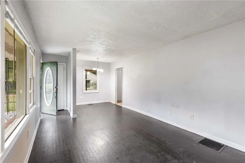 Empty room with a chandelier, a textured ceiling, and dark wood-style flooring
